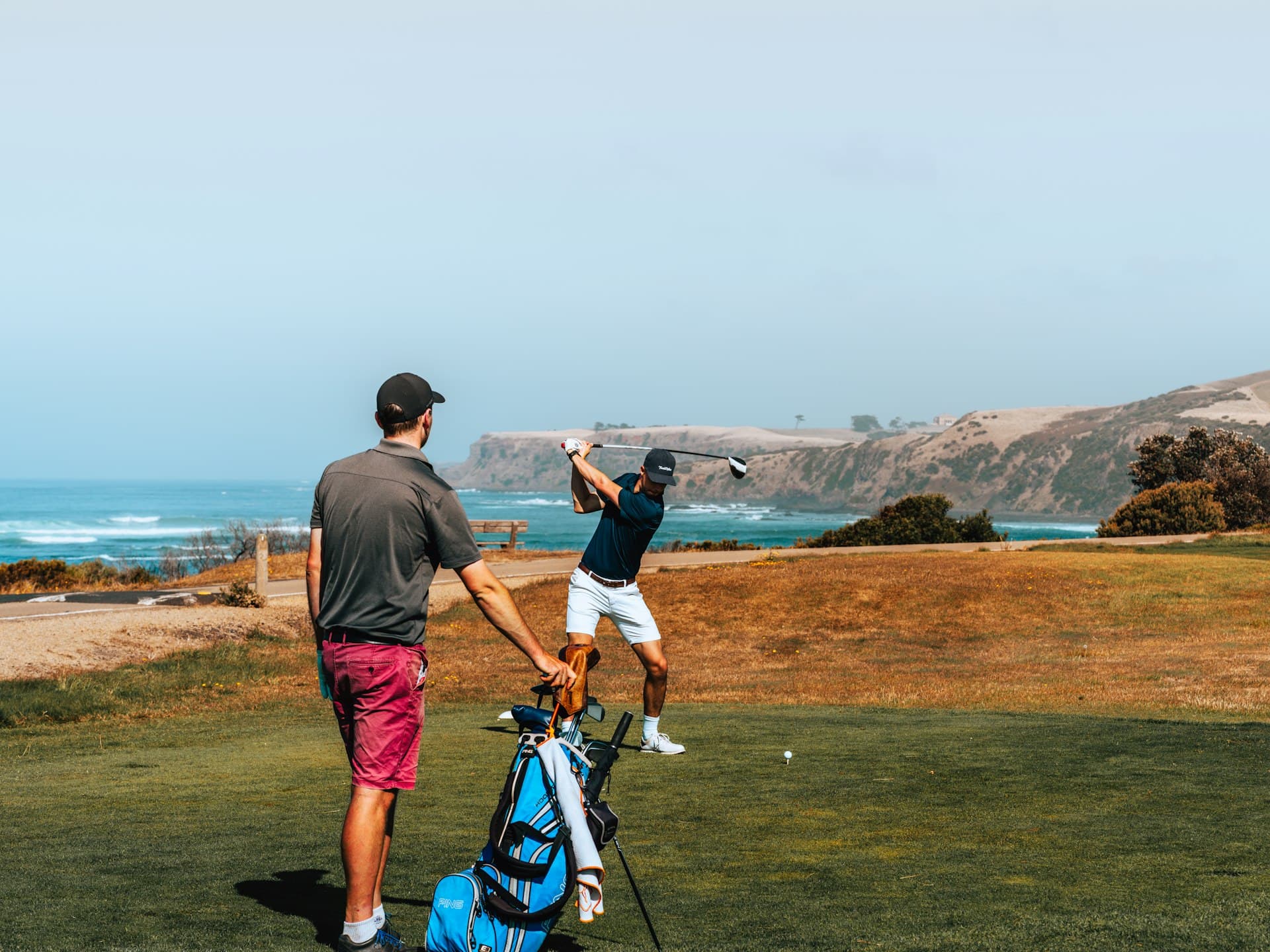 A caddie carrying the bag while a golfer tees off